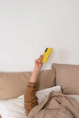 Hand holding smartphone in bed