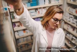 Chemist looking at prescription while searching prescribed drug on shelves in pharmacy 0Ky9V4