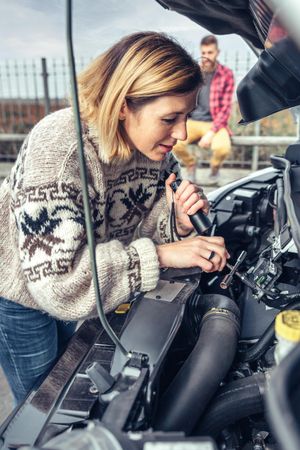 Female in woolen sweater working on car engine