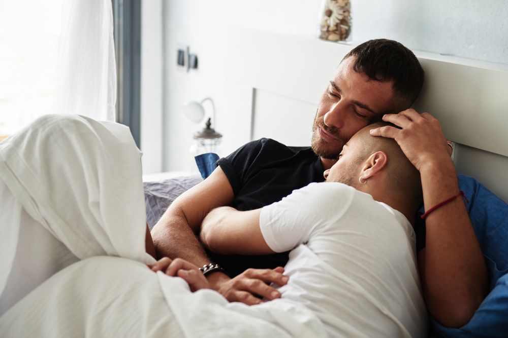 Smiling gay couple hugging on bed