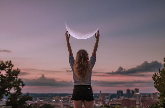 Woman holding her arms up toward the crescent moon