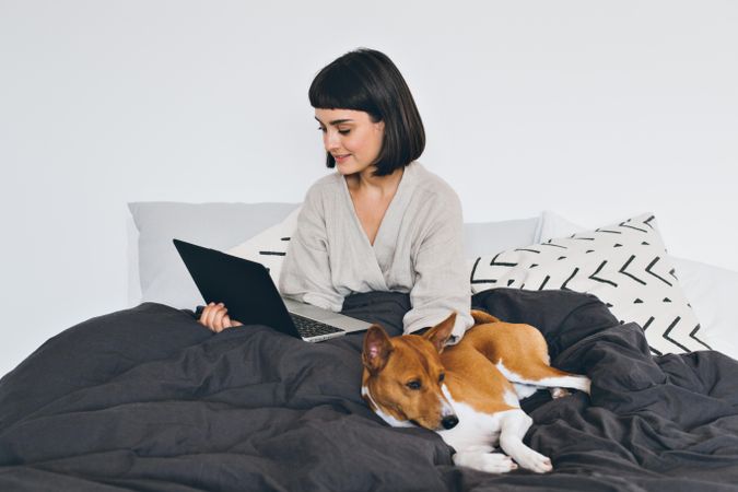 Woman works from home on laptop in bed with dog