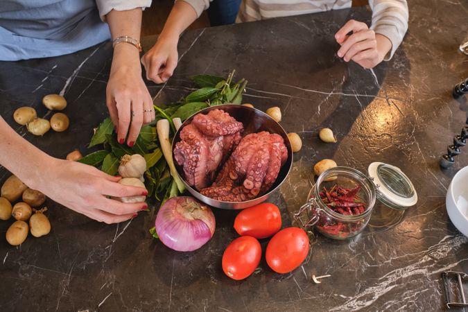 Faceless couple cooking at table with raw octopus