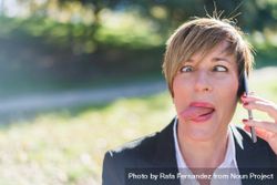 Businesswoman making silly face and talking on cellphone in park 0LzeX4