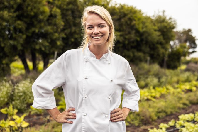 Self-sustainable female chef smiling at the camera cheerfully in an agricultural field