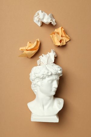 Marble bust with crumpled paper coming out of brain on brown background, vertical