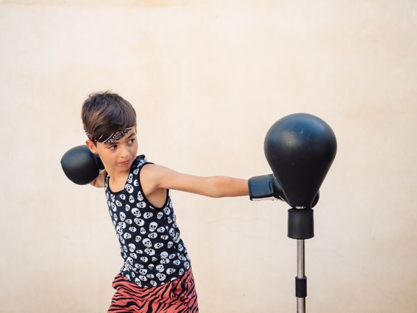 Sporty boy in boxing gloves beating punch bag