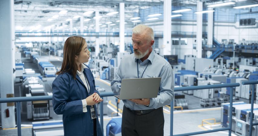 Industrial Engineers Working at a Technology Factory. White Man and Japanese Female Using Laptop Computer and Having a Conversation. Portrait of a Couple at Work