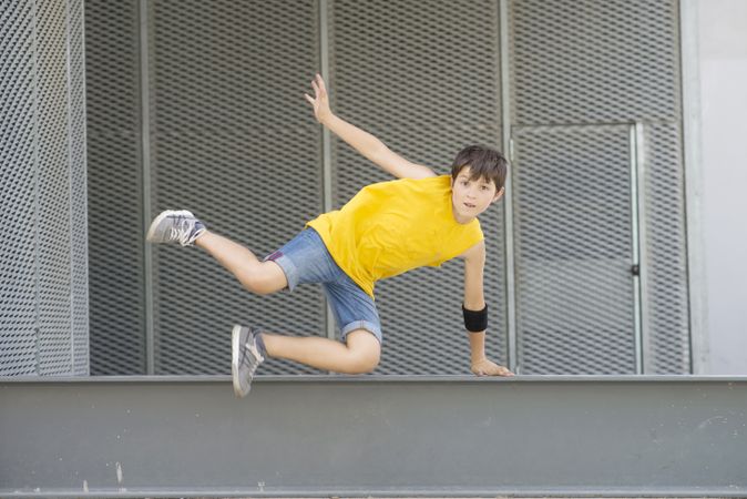 Young teen wearing yellow T-shirt and jumping over rail