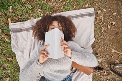 Black woman hiding face behind book in nature