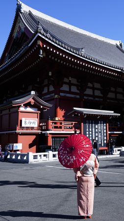 Back view of a woman in kimono holding an umbrella standing near Senso-ji Buddhist temple in Japan