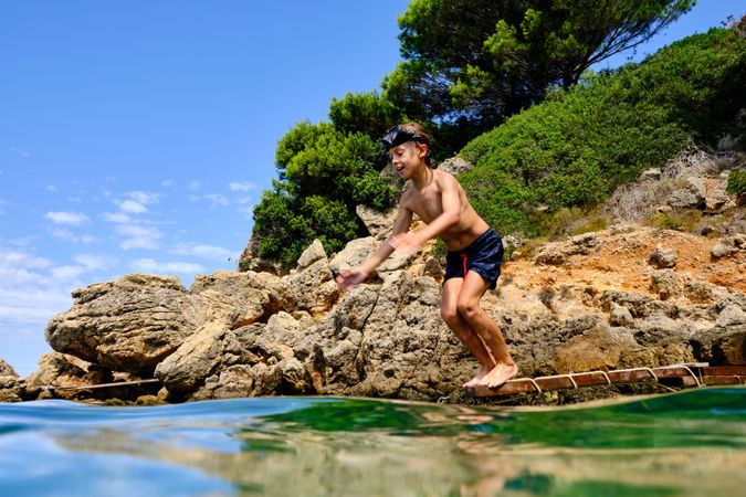 Shirtless boy diving into water from wooden plank