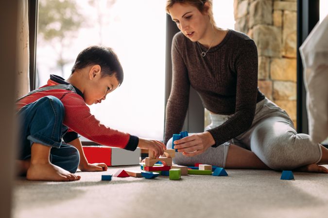 Mother and son playing with colorful toys at home on the floor