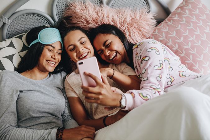 Young women lying on bed laughing while looking at a mobile phone