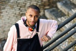 Male in overalls and hoodie leaning on railing of stairs outside
