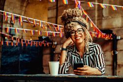 Happy Black woman in stripe shirt texting in cafe
