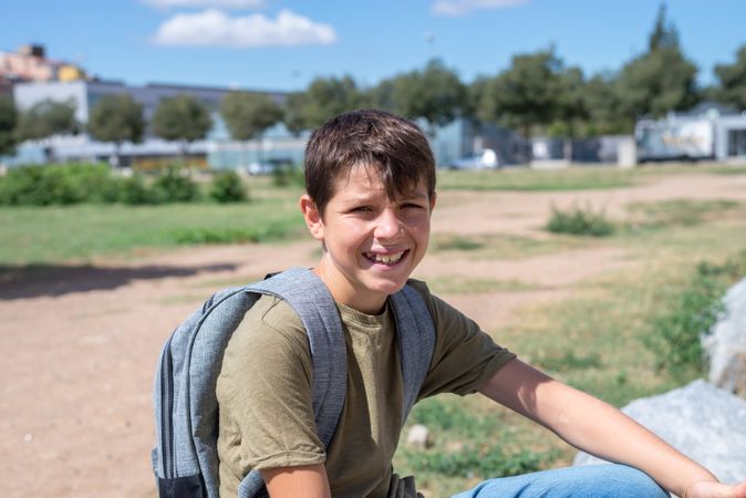 Smiling boy sitting on outside with backpack
