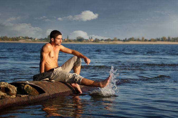 Male sitting down on rocks around a lake