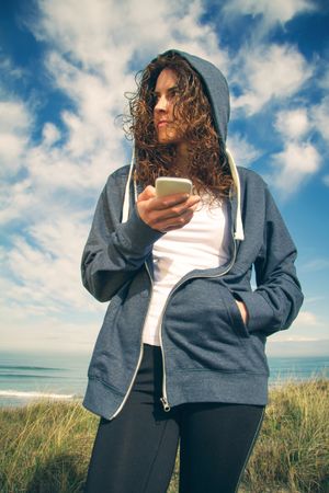 Woman checking phone with ocean in background, vertical
