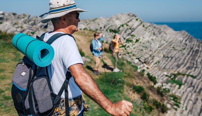 Older man in foreground of his family taking photos of the view while hiking