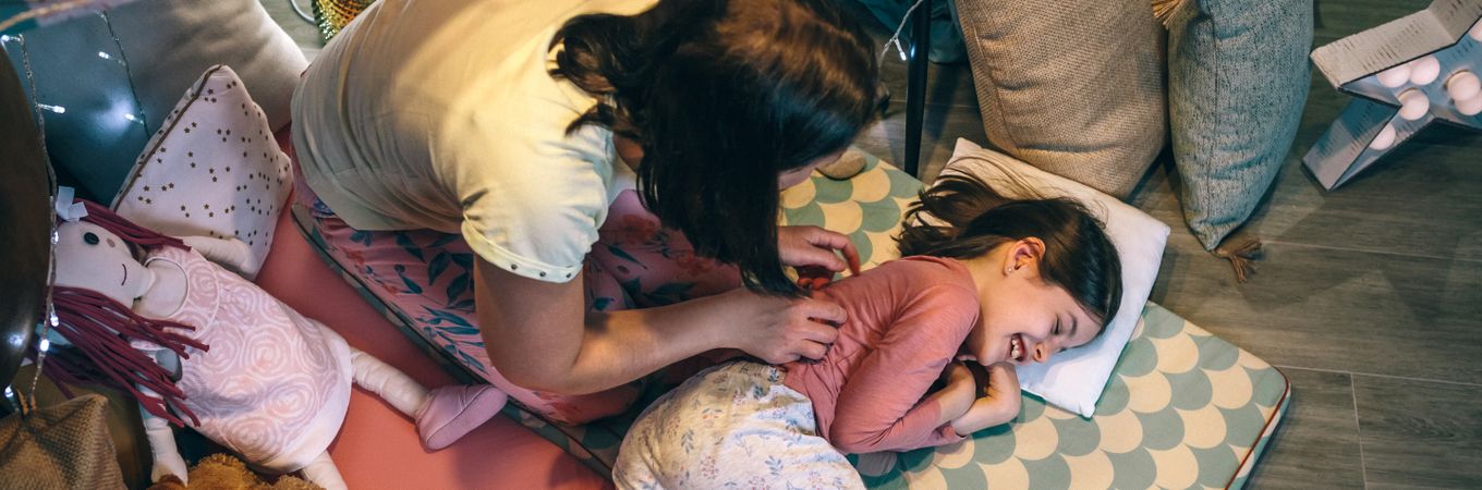 Banner of woman waking up a smiling young girl lying over mats. Single parent family leisure concept