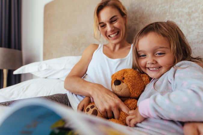 Happy mother and daughter looking at a book and smiling on bed