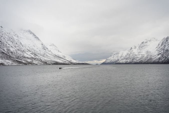 Tranquil lake against snowy hills in cold overcast weather