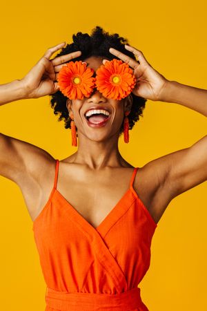 Joyful Black woman holding two flowers over her eyes