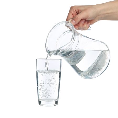 Hand pouring water in glass from pitcher in blank studio