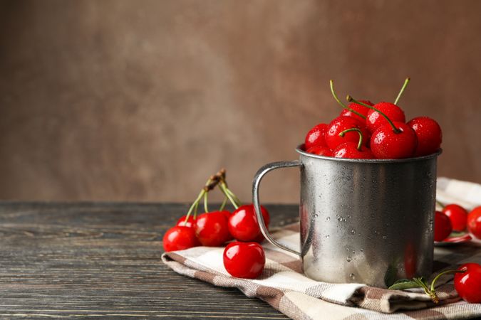 Towel and metal mug with cherry on wooden background. Summer plant