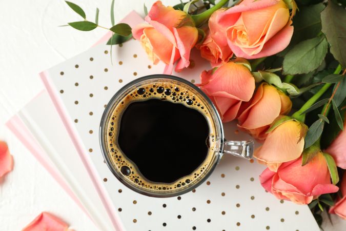 Composition with cup of coffee, notebooks and pink roses on plain background, top view