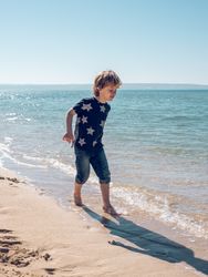 Content boy walking on sunny coast of sea