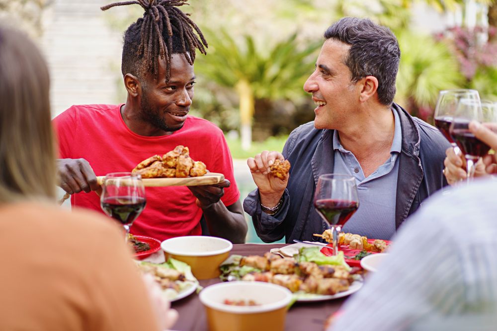 Happy multi-ethnic friends sitting at farmhouse table sharing a plate of chicken