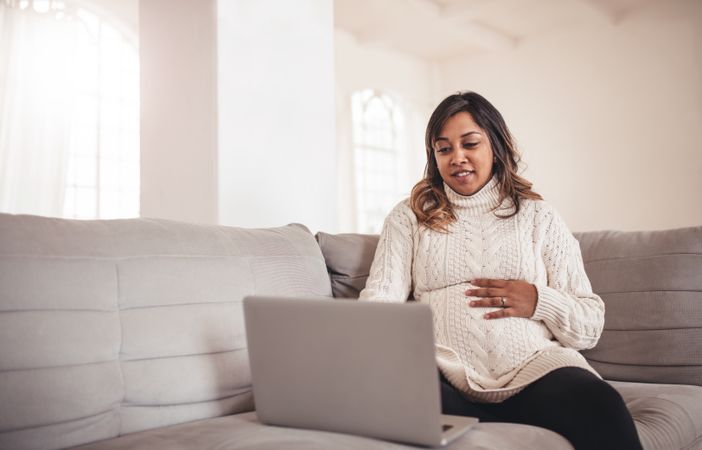 Portrait of beautiful young pregnant woman with laptop sitting on couch