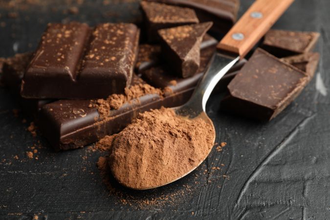 Tasty chocolate and spoon with powder on dark background