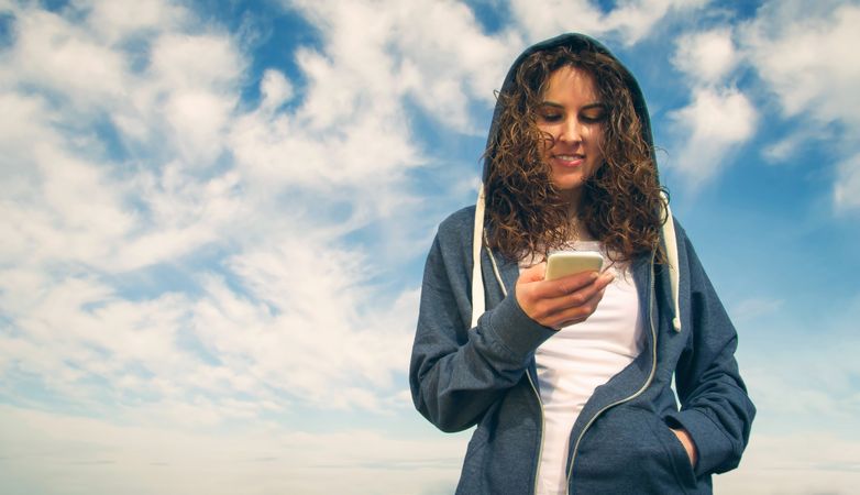 Woman checking phone with beautiful blue and cloudy sky in background