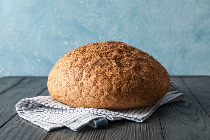 Bread on kitchen towel on wooden table against light background, space for text