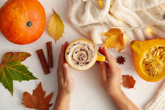 Composition with female hands hold pumpkin latte on light background