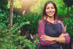 Confident smiling woman pictured in a greenhouse with her arms crossed