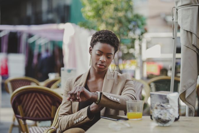 Black woman checking time and sitting at table with smartphone in cafe