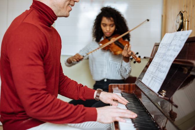 Man playing piano near woman playing violin in studio