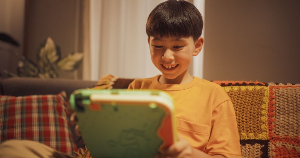 Medium Portrait of a Happy Excited Kid Using Tablet Computer in the Living Room at Home.