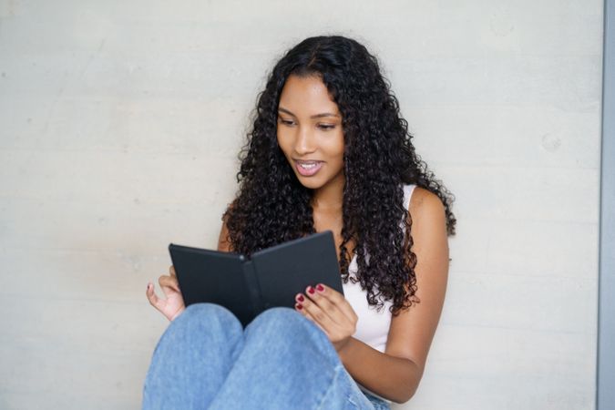 A Young Woman Deeply Engrossed in Reading on Her Tablet While Relaxing at Home Comfortably
