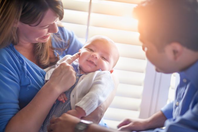 Happy Couple Enjoying Their Newborn Son In The Light of The Window.