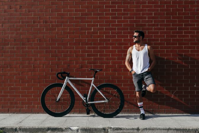 Sportive man standing next to brick wall with bike