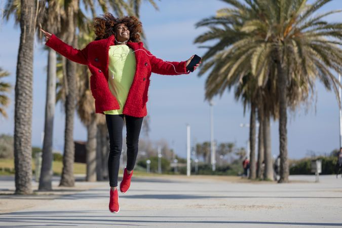 Female jumping with open arms while listening to music in front of palm trees