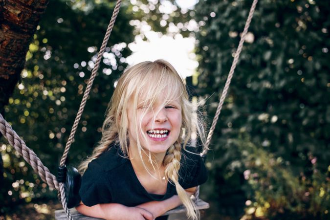 Smiling blonde girl with braided hair leaning on outdoor swing