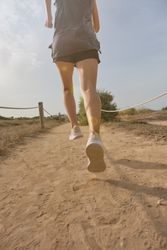 Unrecognizable woman jogging on sandy road