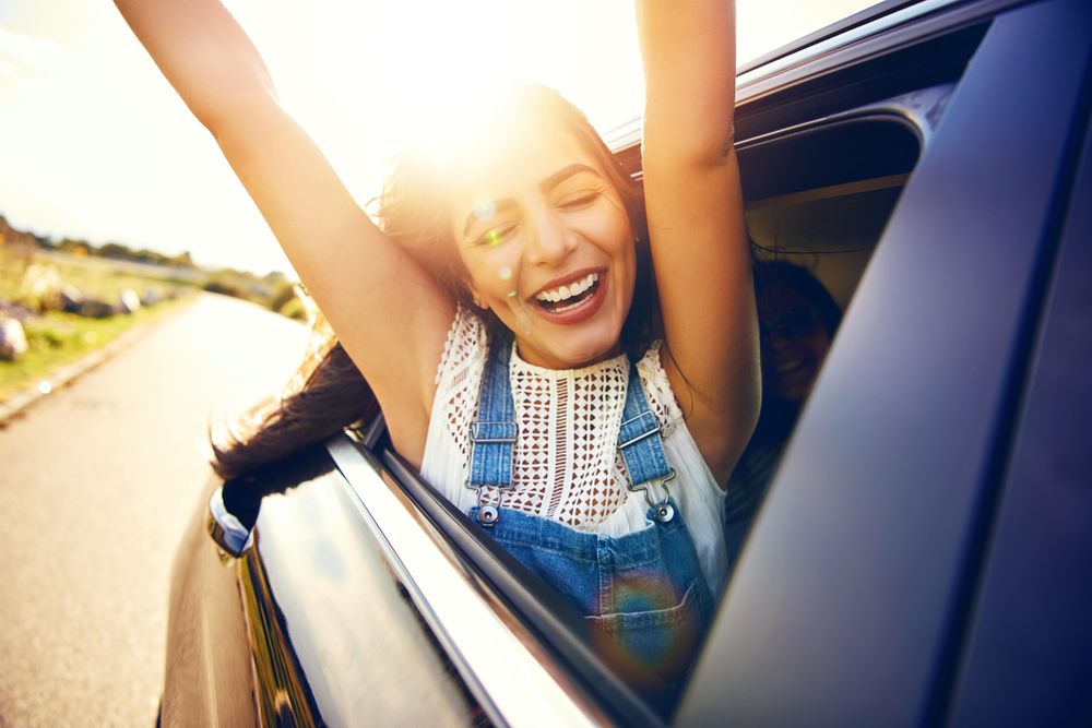 Happy female with arms outstretched outside of car window