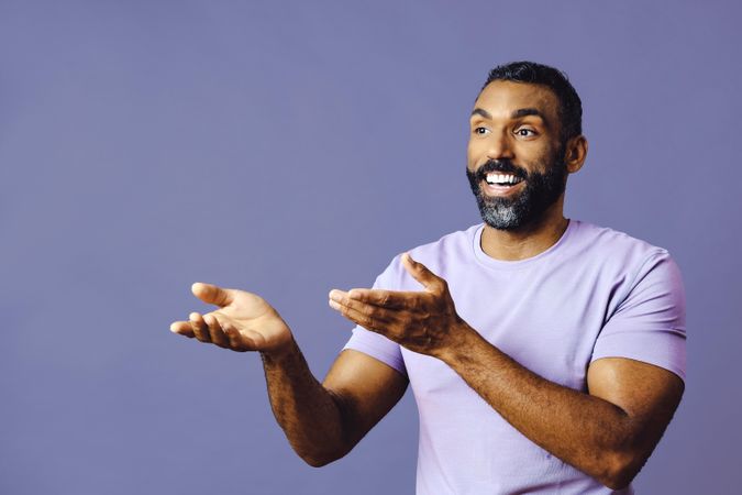 Male speaking in purple t-shirt with hands gesturing to copy space in purple studio